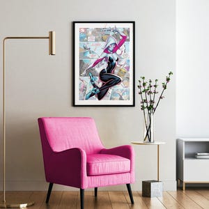 May include: A framed comic book art print featuring a female superhero in a white and black costume with a red spider symbol on her chest. The superhero is in mid-air, kicking with her right leg and holding her left arm out. The background is a comic book panel with a cityscape and other superheroes.