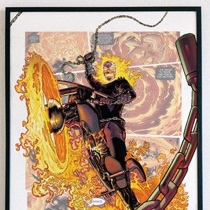 May include: A framed comic book art print featuring Ghost Rider, a superhero with a flaming skull, riding a motorcycle with a chain attached to the frame. The print is surrounded by a black frame.