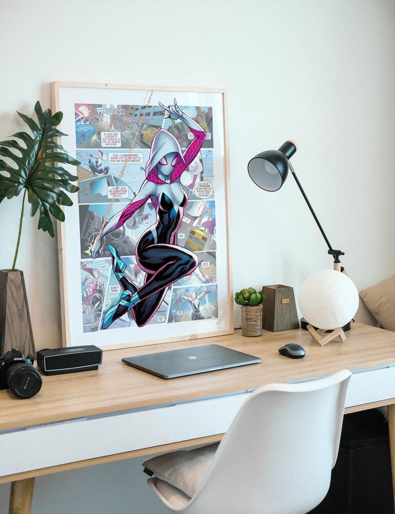 May include: A framed comic book poster featuring a female superhero in a white and black suit with pink accents. She is swinging from a web and has a white mask with a spider design. The poster is hanging on a white wall above a desk with a laptop, a lamp, and a white chair.
