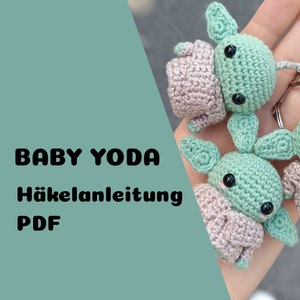 Könnte beinhalten: Zwei gehäkelte Baby Yoda Amigurumi-Spielzeuge, eines in Grün und eines in Beige, mit großen schwarzen Augen. Die Spielzeuge werden in einer Hand gehalten. Der Text "BABY YODA Häkelanleitung PDF" ist im Bild sichtbar.