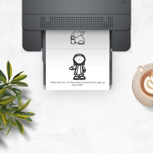 May include: A printer is shown with a printed page featuring a cartoon illustration of a person and the text "Peter told him, in the name of Jesus Christ, get up and walk!" A cup of coffee with latte art is on the right.