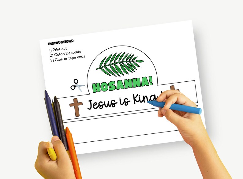 May include: A printable crown template with the words "HOSANNA!" and "Jesus is King" in a playful font. The image shows a child's hand coloring the template with a blue crayon. Other crayons are visible.