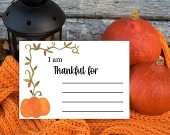 May include: A white card with a vine border and the text "I am Thankful for" with lines for writing. The card is on a knitted orange blanket with two orange pumpkins.