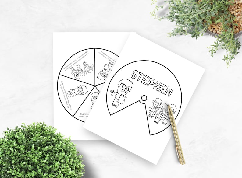 May include: Two white paper cutouts with black line drawings. One cutout is a circle divided into sections with illustrations and text. The other cutout has the name "STEPHEN" and a drawing of a man. A gold pen rests on the paper.