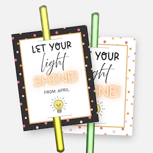 May include: Two rectangular cards with the text "LET YOUR light SHINE!" and a lightbulb illustration. The cards have a black border with pink polka dots and are held by a yellow and green clip.