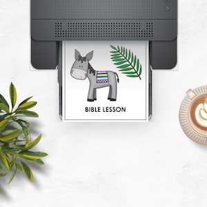May include: A printer is shown printing a page with a cartoon donkey, a green palm branch, and the words "BIBLE LESSON". A cup of coffee with latte art is on the right. A green plant is in the lower left corner.