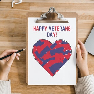 K&ouml;nnte beinhalten: Ein Klemmbrett mit einem wei&szlig;en Blatt Papier mit dem Text "HAPPY VETERANS DAY!" in Rot und einem Herzdesign, das mit roten und blauen Pinselstrichen gef&uuml;llt ist. Eine Hand h&auml;lt einen Bleistift, und ein Laptop ist sichtbar.