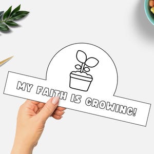 May include: A black and white paper craft with the text "MY FAITH IS GROWING!" and a potted plant illustration. Gold scissors and a sprig of greenery are in the background, along with a bowl of heart-shaped candies.