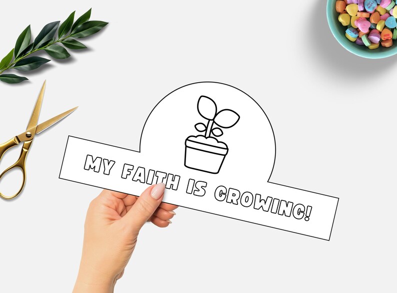 May include: A black and white paper craft with the text "MY FAITH IS GROWING!" and a potted plant illustration. Gold scissors and a sprig of greenery are in the background, along with a bowl of heart-shaped candies.