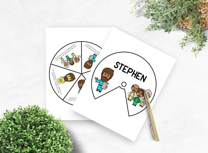 May include: Two white cards with illustrations and text. One card has a circular design with segmented illustrations and text. The other card has the name "STEPHEN" in a circle with an illustration. A gold pen rests on the card.