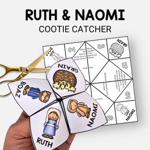 May include: A white paper cootie catcher with the text "RUTH & NAOMI" and illustrations of characters. A pair of gold scissors rests beside the folded paper game. The game includes questions and answers.