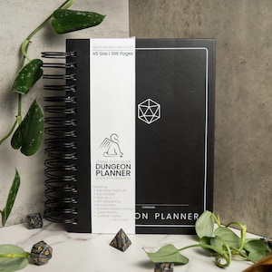 May include: A black A5 size Dungeon Planner with 396 pages. The cover features a white d20 dice symbol and the text "SPHINK STATIONERY DUNGEON PLANNER" with the words "CAMPAIGN" and "ON PLANNER" at the bottom.