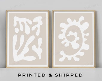 May include: Two framed prints with abstract white shapes on a beige background. The prints are in a light wood frame and are hung on a white wall. The text "PRINTED & SHIPPED" and "VUDORA GICLEE // ON ETSY" is below the prints.