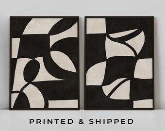 May include: Two black framed prints featuring abstract geometric shapes in black and white. The prints are hung on a white wall. The text "PRINTED & SHIPPED" and "VUDORA GICLEE // ON ETSY" is below the prints.