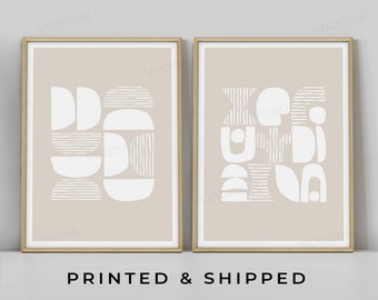May include: Two beige framed prints with white abstract geometric shapes on a light beige background. The prints are on a white surface.