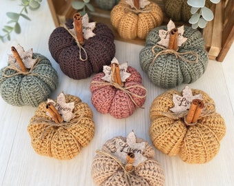 May include: Eight crocheted pumpkins in various colors, including brown, green, pink, and yellow. Each pumpkin has a cinnamon stick and a small leaf tag with the word "Liven" on it.