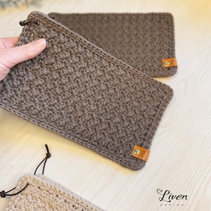 Peut inclure: Deux pochettes en crochet marron et beige avec des lanières en cuir et des étiquettes en cuir marron qui disent "Liven Design".
