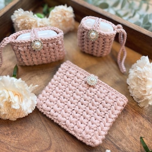 Può includere: Tre custodie in crochet rosa con decorazioni di perle. Le custodie sono progettate per contenere piccoli oggetti come auricolari o gioielli.