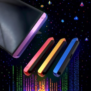 Pode incluir: Um smartphone com uma capa roxa e três capas de telefone coloridas em vermelho, amarelo e azul. As capas têm um interior preto e um acabamento metálico. O fundo apresenta um tema espacial pixelizado com detalhes coloridos.
