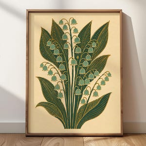 May include: A framed botanical print featuring a stylised illustration of lily of the valley flowers with light blue bell-shaped blossoms and dark green leaves with gold-coloured stippled details on a cream-coloured background.