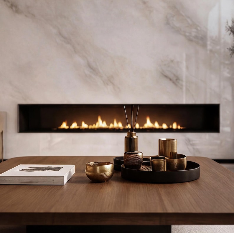 May include: A wooden coffee table displays decorative items. A gold bowl, a black tray with gold-colored cups, and a book are arranged on the table. A fireplace with flames is in the background.