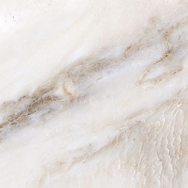 May include: Close-up of a white marble surface with subtle brown and gray veining. The natural stone has a polished appearance, with variations in color and texture. The overall effect is a smooth, elegant, and luxurious look.