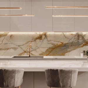 May include: Modern kitchen design featuring a marble countertop and backsplash with gold and brown veining. Overhead, sleek, linear light fixtures illuminate the space. Two gray velvet chairs are positioned at the counter. The kitchen cabinets are a light gray color.