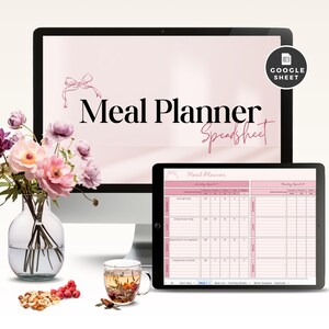 Könnte beinhalten: Ein Desktop-Computer und ein Tablet zeigen eine rosa Essensplaner-Tabelle. Der Computerbildschirm zeigt "Meal Planner Spreadsheet" in schwarzer und rosa Schrift. Eine Vase mit rosa Blumen, eine Tasse Tee und eine Schüssel mit Nüssen und Beeren befinden sich im Vordergrund.