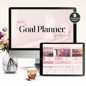 May include: A desktop computer and tablet display a pink Goal Planner Spreadsheet. The computer screen shows the title with a bow graphic. The tablet displays a detailed goal checklist. A glass mug of tea and a vase of flowers are in the foreground.