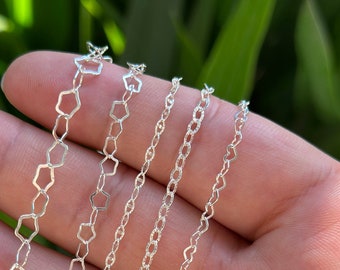 May include: Five silver chains of different styles and lengths. The chains are arranged in a fan shape on a hand.