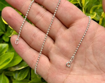 May include: A silver ball chain necklace with a lobster clasp closure. The chain is made of small, round beads.