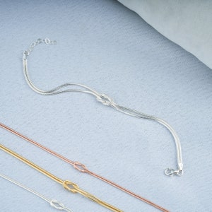 Pode incluir: Tr&ecirc;s pulseiras de corrente prateadas com um design de n&oacute;. A pulseira superior &eacute; uma corrente dupla, a pulseira do meio &eacute; uma corrente simples e a pulseira inferior &eacute; uma corrente dupla.