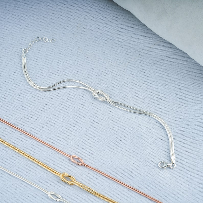 Pode incluir: Tr&ecirc;s pulseiras de corrente prateadas com um design de n&oacute;. A pulseira superior &eacute; uma corrente dupla, a pulseira do meio &eacute; uma corrente simples e a pulseira inferior &eacute; uma corrente dupla.