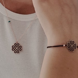 以下が含まれることがあります： ローズゴールドのネックレスとブレスレットのセット。ケルトノットのデザインが特徴です。ネックレスには、詳細なノットと小さな緑色のビーズが付いたペンダントが付いています。ブレスレットには、暗いコードにマッチするノットチャームが付いています。