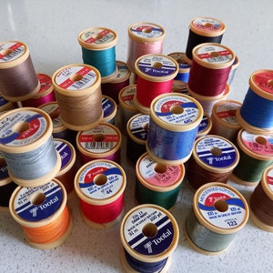 May include: A selection of multi-coloured cotton thread spools, including shades of brown, blue, and red. Each spool displays the "Tootal" brand and the thread length, which is 91 meters. The spools are arranged in a pile.