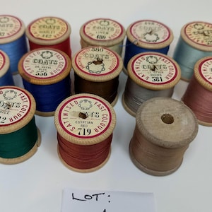 May include: A collection of twelve wooden spools of Coats machine twist thread in various colours including blue, red, green, brown, and grey. Each spool features a circular paper label on top with the brand name, colour name, and number.