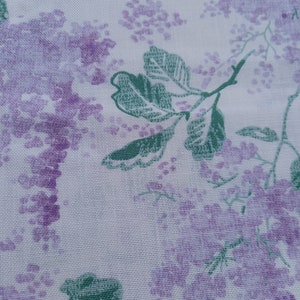 Op de afbeelding: Witte stof met een bloemenpatroon met paarse bloemen en groene bladeren.
