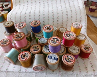 May include: A collection of wooden spools of thread in various colors, including red, blue, green, yellow, and white. The spools are labeled with the brand name "Stikko" and other details about the thread.