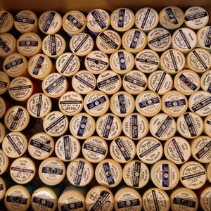 May include: A collection of spools of thread in various colours, each with a label that includes the brand name "SYLKO" and a colour name. The spools are arranged in a grid pattern.