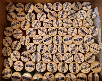 May include: A collection of spools of thread in various colors, each with a label that includes the brand name "SYLKO" and a color name. The spools are arranged in a grid pattern.