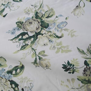 Op de afbeelding: Witte stof met een bloemenpatroon met rozen, blauwe bloemen en groene bladeren. Het ontwerp heeft een vintage esthetiek, met zachte kleuren en een delicate rangschikking van botanische elementen. Ideaal voor stof of behang.