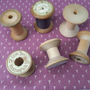 May include: A collection of vintage wooden spools, some with remnants of thread. One spool has a label that reads "Extra Qual. Pearl's Knitting Silk". The spools are various sizes and shapes, with a natural wood finish.