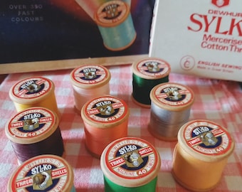 May include: A collection of ten spools of thread in various colors, including orange, green, blue, and brown. Each spool is labeled "Dewhurst's Sylko Three Shells Machine 40 Twist".