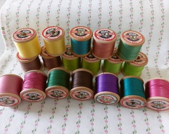 May include: A collection of 18 vintage wooden spools of thread in various colors, including red, green, purple, brown, and yellow. Each spool has a label that reads "Sylko Triple Sheens 40".