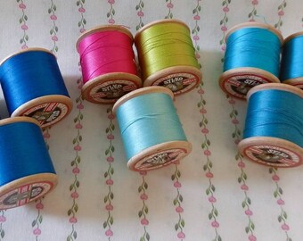May include: Assortment of ten spools of thread in various colors, including blue, green, pink, and turquoise. The spools are made of wood and have a white label with the word "Stylo" printed on them.
