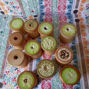 Pode incluir: Uma coleção de carretéis de fio de madeira com etiquetas verdes e brancas. As etiquetas têm o texto "Lustre" e "Machine Twist". Alguns carretéis têm o texto "J&P Coats" e "100 yds".