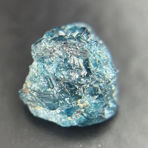 Op de afbeelding: Een ruwe, donkerblauwe edelsteen met een gefacetteerd oppervlak. De edelsteen is een natuurlijk kristal met een unieke, onregelmatige vorm.