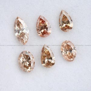 May include: Six loose faceted gemstones in various shapes, including marquise, pear, and oval cuts. These stones exhibit a warm, light brown champagne color with brilliant internal reflections and sharp, symmetrical facets throughout each piece.