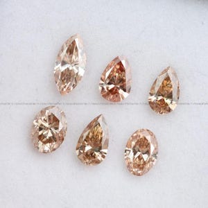 May include: Six loose faceted gemstones in shades of champagne and light brown. The collection includes two oval-shaped stones, two pear-shaped stones, one marquise-cut stone, and one teardrop-shaped stone, all featuring intricate geometric facets.