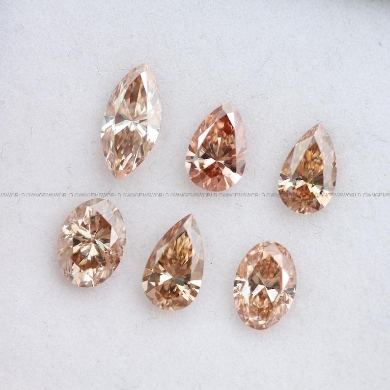 May include: Six loose faceted gemstones in shades of champagne and light brown. The collection includes two oval-shaped stones, two pear-shaped stones, one marquise-cut stone, and one teardrop-shaped stone, all featuring intricate geometric facets.